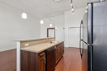 A kitchen with a black dishwasher,  refrigerator and wooden cabinets.